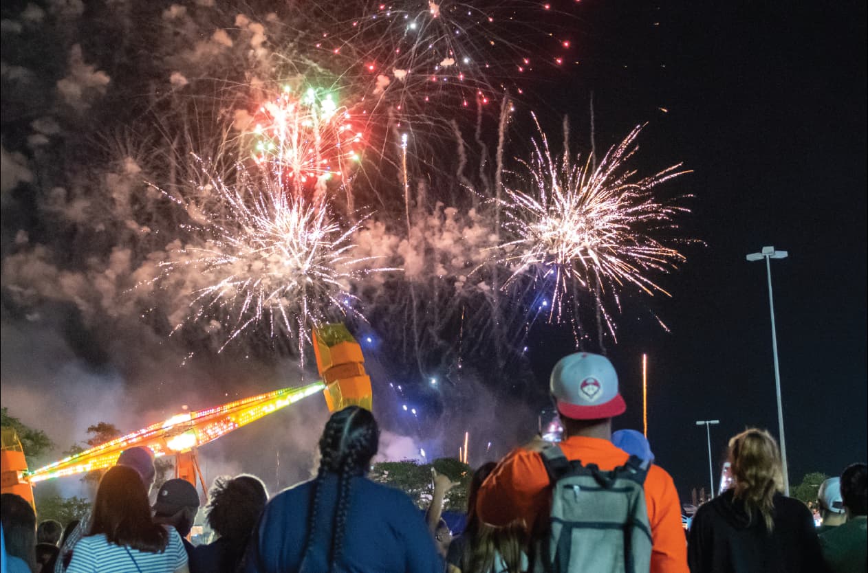 People watching fireworks over carnival ride